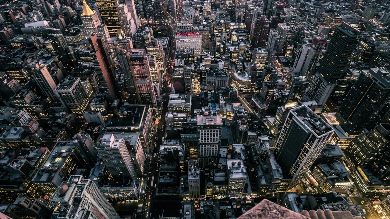 A birds-eye view of a business district of a bustling metropolitan downtown, illuminated by traffic and the lights from skyscrapers.