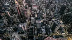 A birds-eye view of a business district of a bustling metropolitan downtown, illuminated by traffic and the lights from skyscrapers.